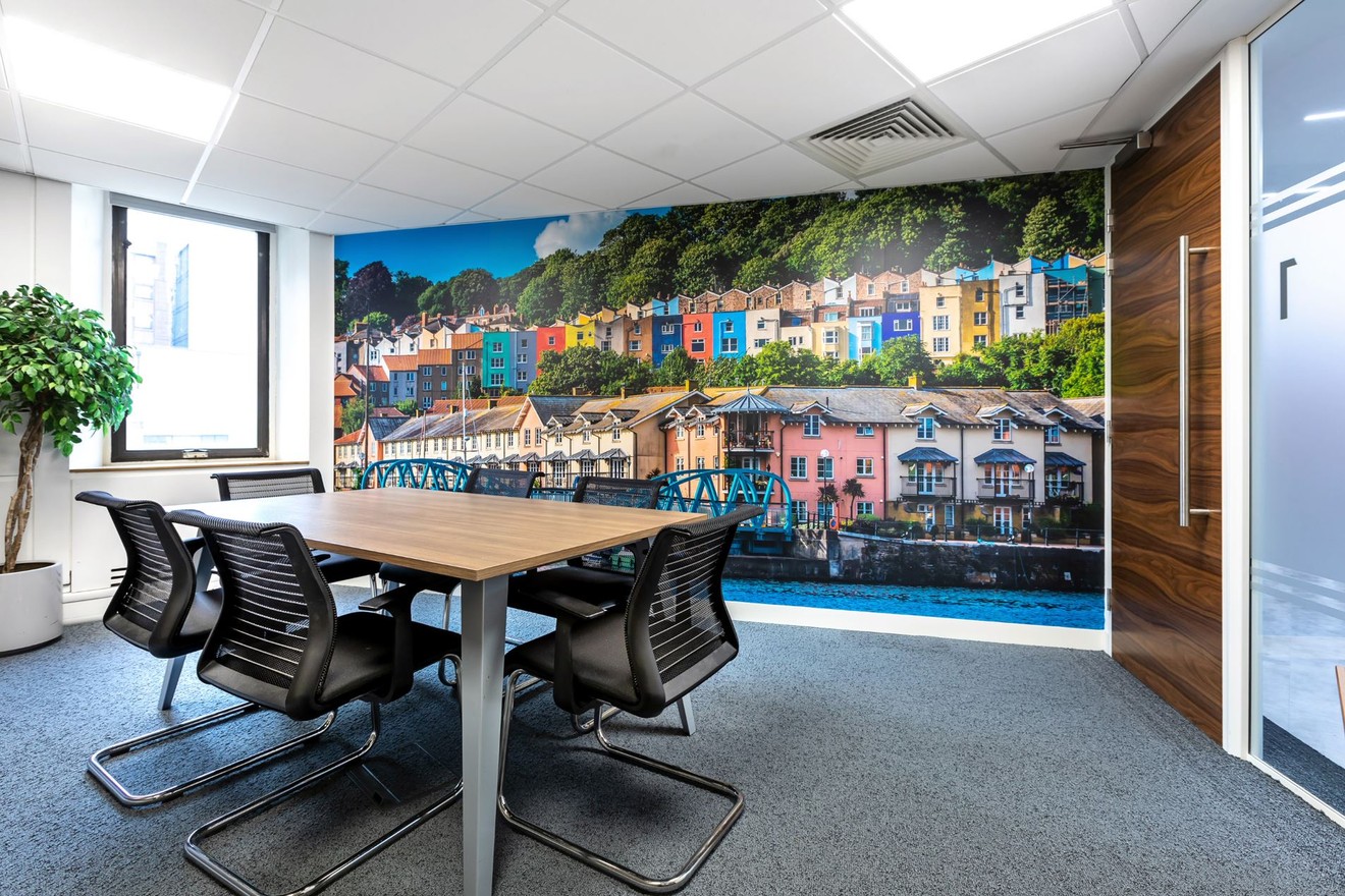 A meeting room with a table and chairs and a bespoke feature wall with an image of houses, a bridge and a river.