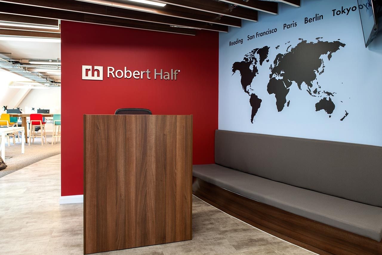 A reception area with small desk, a sofa and a blue feature wall with a map on it.