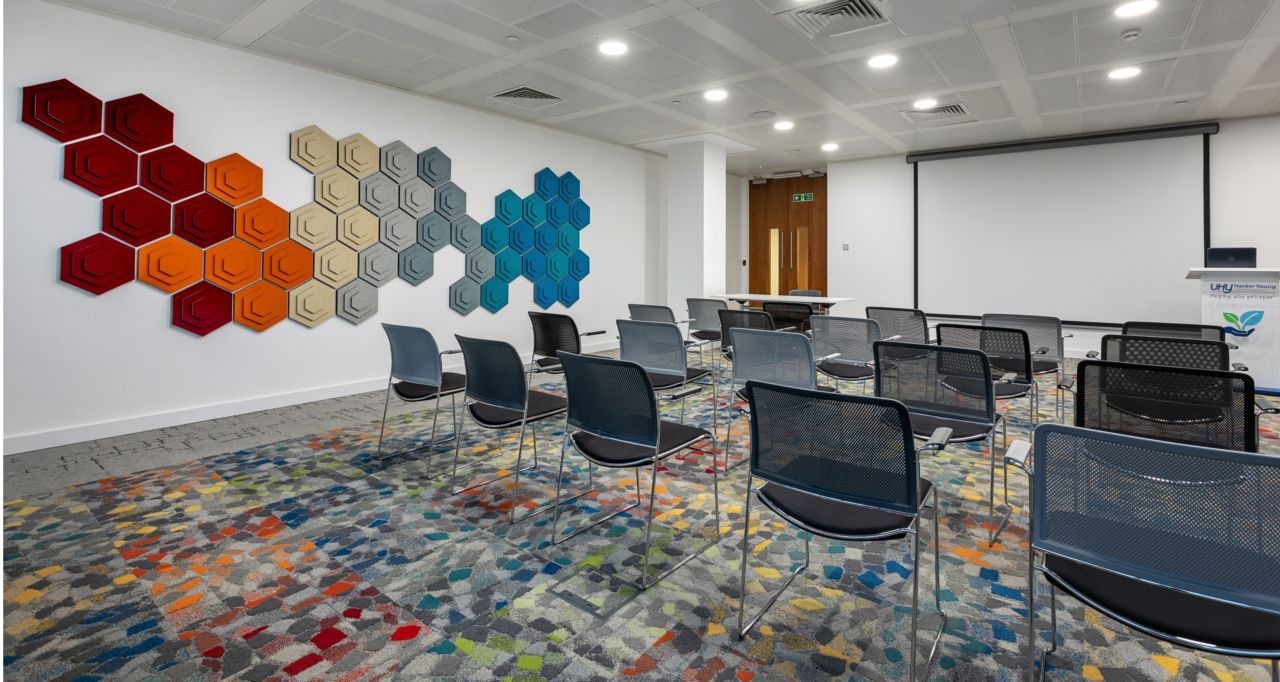 An office auditorium room with a projector, speakers column and chairs set out in rows.