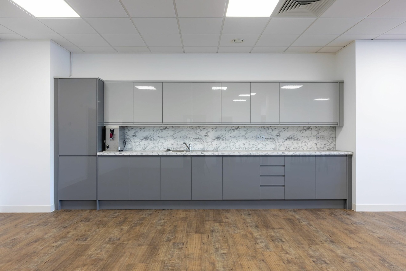 A long kitchenette with dark and light grey cabinets, a coffee machine, marbles work tops and a marble splashback.