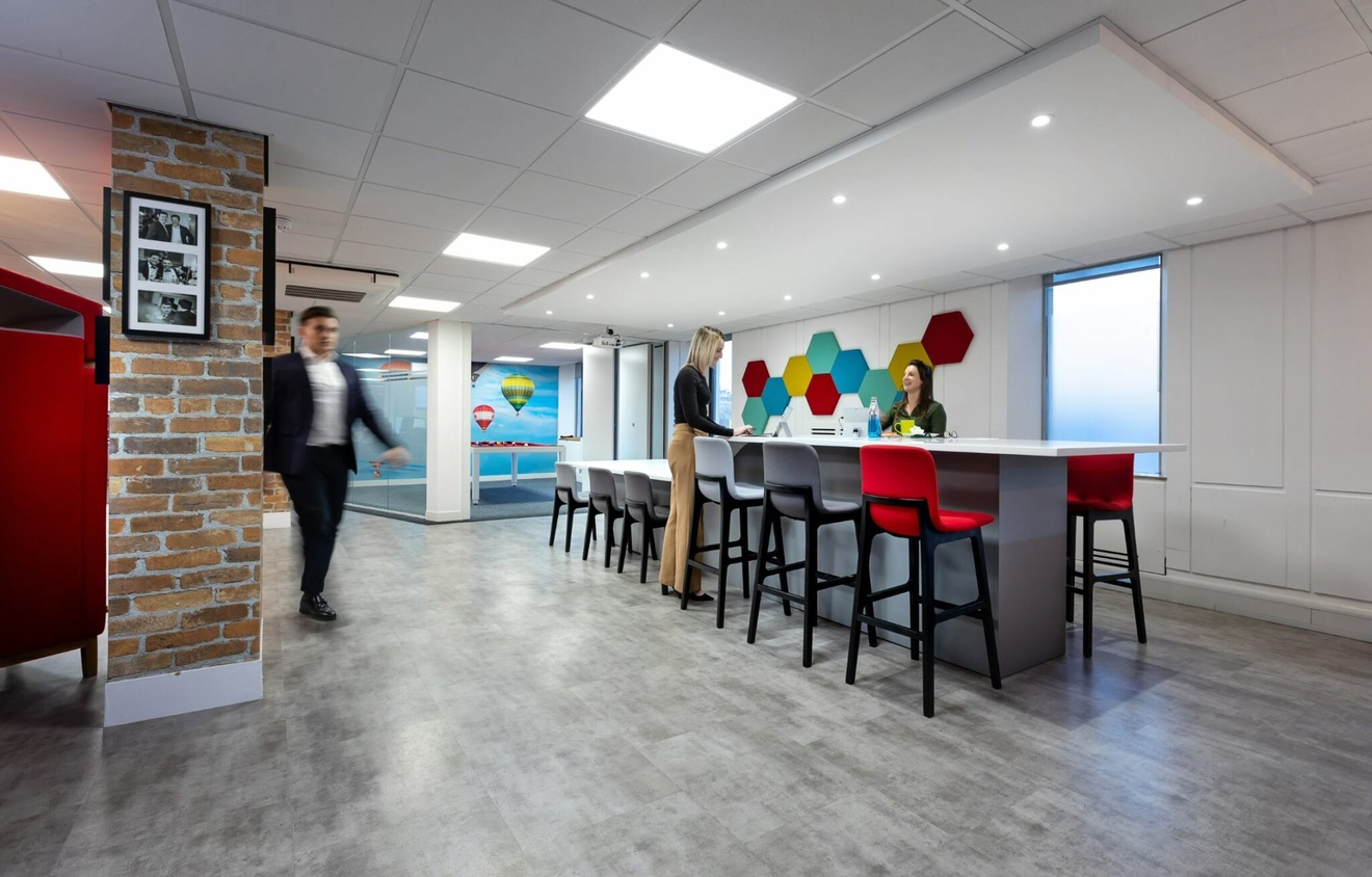 Two people stood at a high table talking and a blurred image of a person walking past.