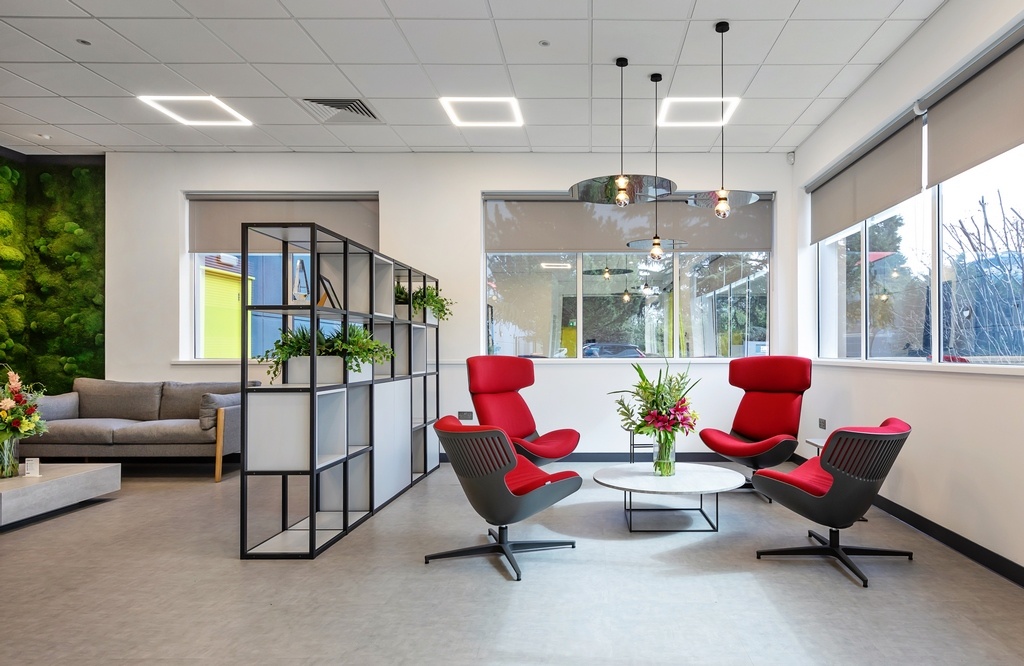 white walled sitting area in an offie with red chairs a grey sofa and large windows