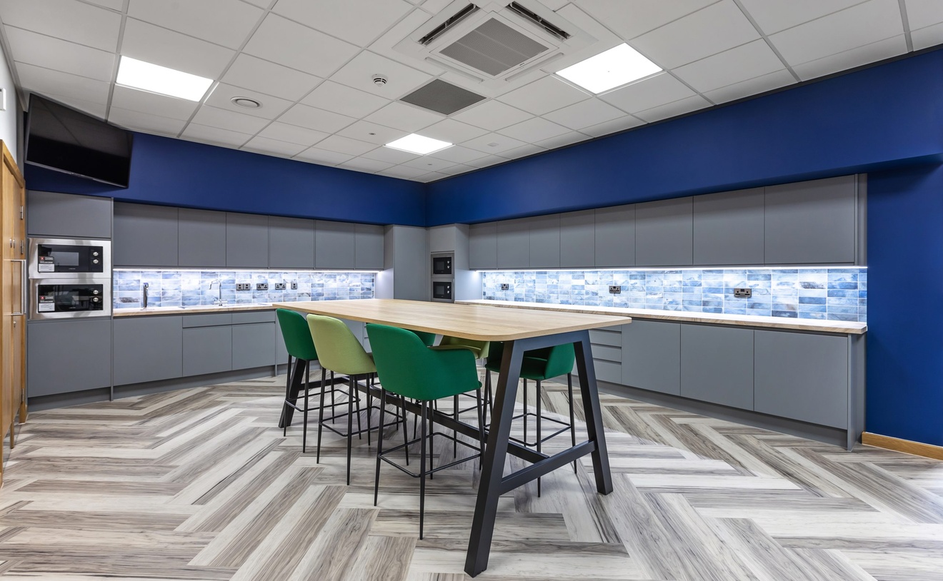 modern grey and blue kitchen with table and high legged green chairs in the centre