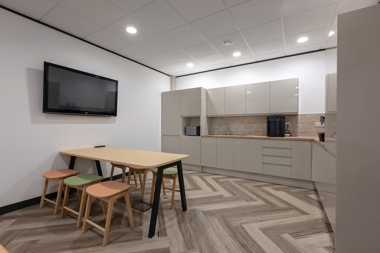 Image of a breakout area - herringbone flooring and grey kitchen cabinets.