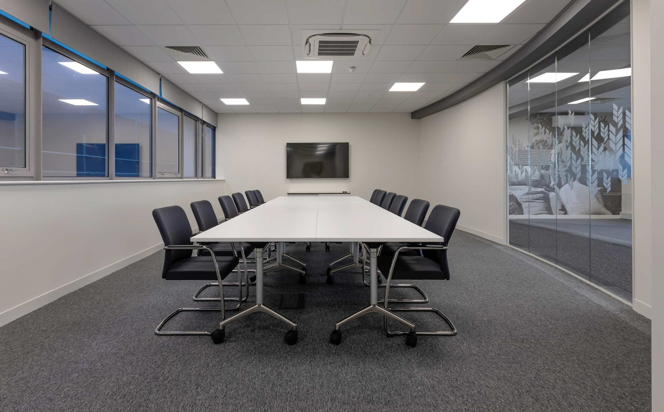A long boardroom with a white meeting table, which is surrounded by multiple chairs.