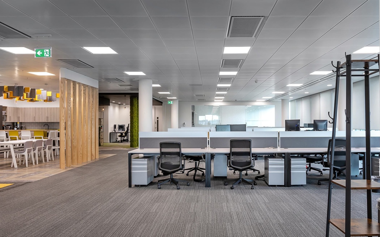 An empty office space with desks, chairs and a kitchenette on the left.