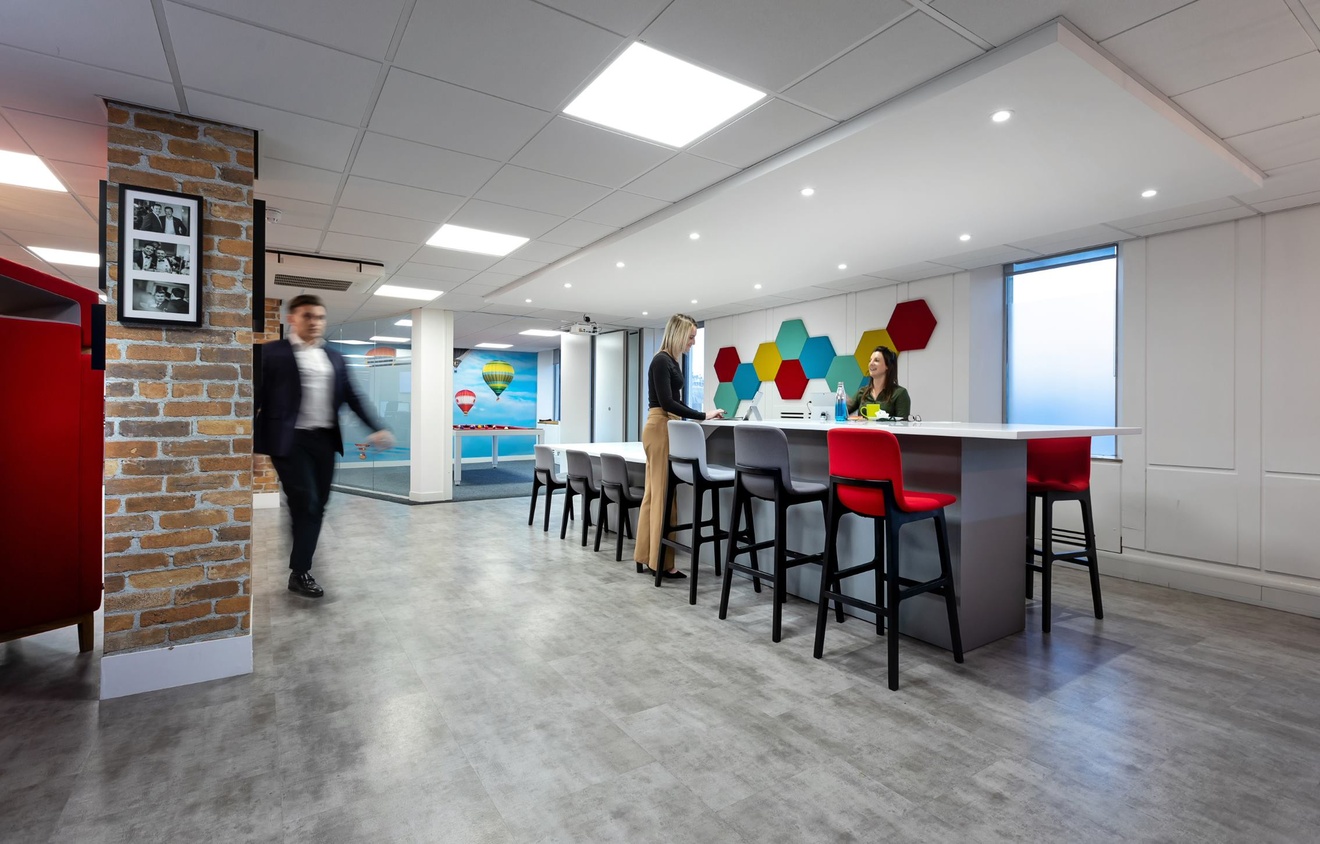 Two people stood at a high table talking and a blurred image of a person walking past.
