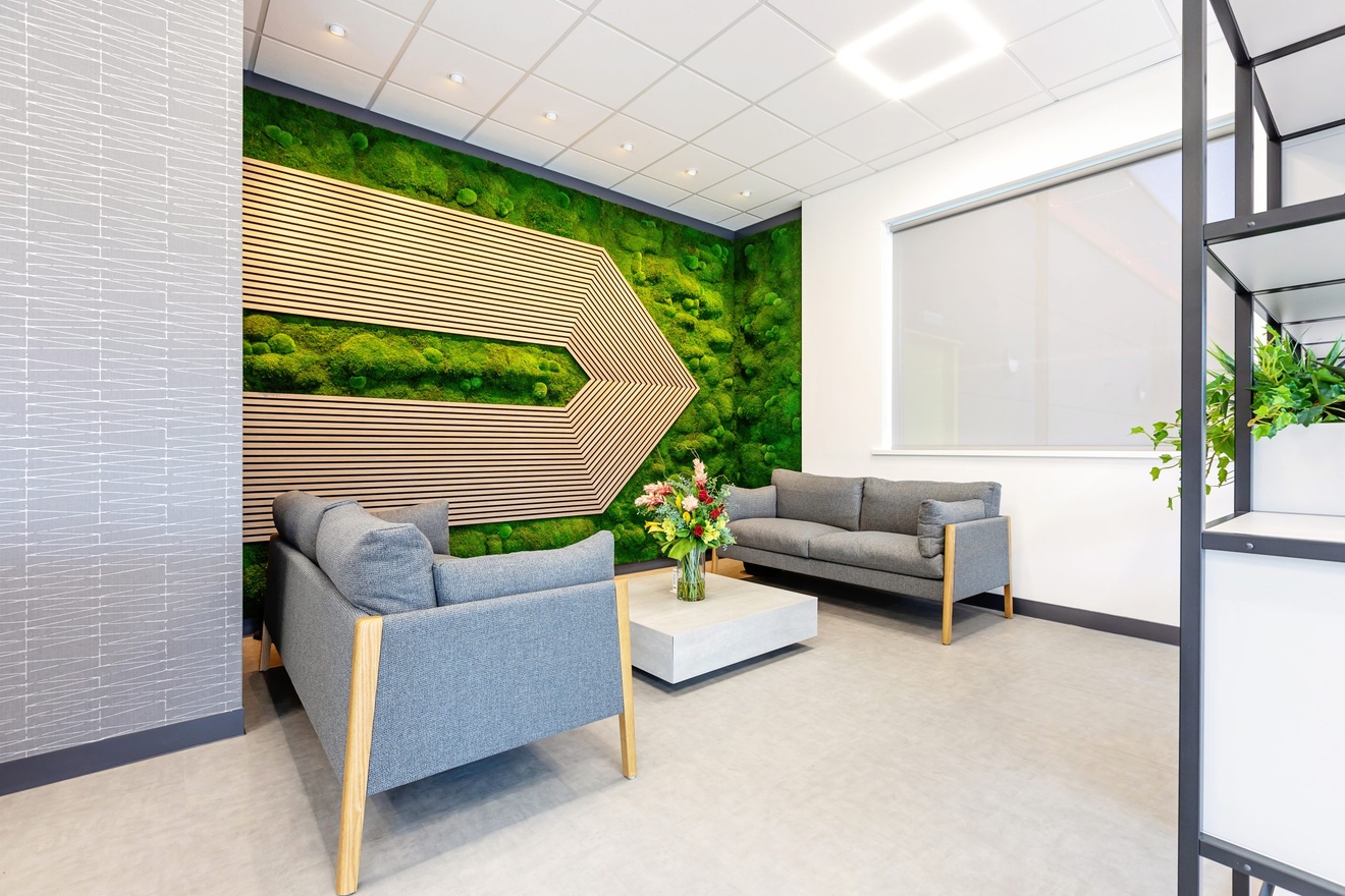 office sitting area with art of trees seen from above on the left wall and grey plush sofas and flowers on the coffee table