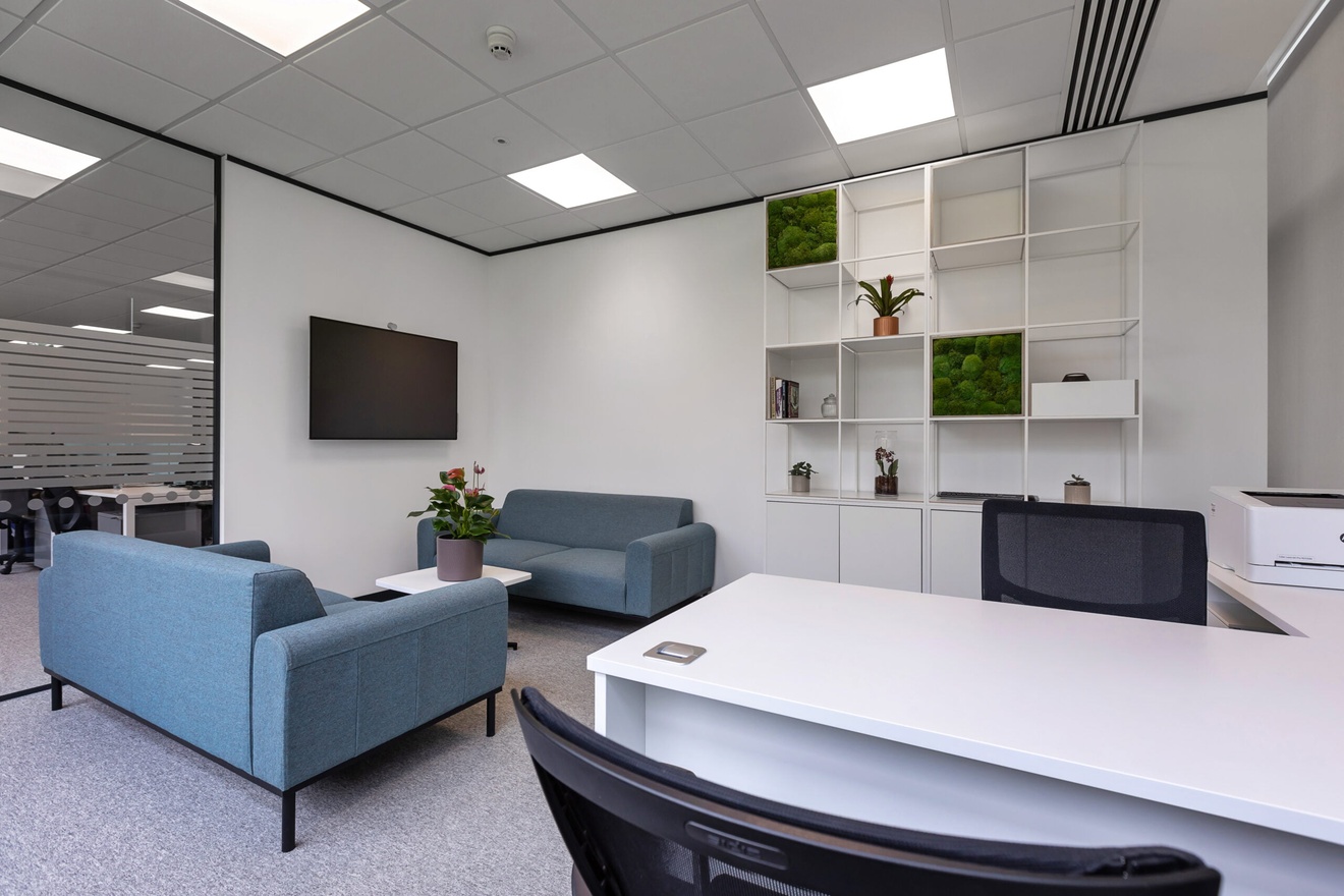 Image of a director's office with blue sofas and a large white desk.