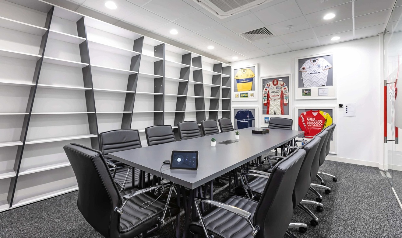 A boardroom with a long table, surrounded by chairs, ample shelving and framed sports jerseys on the wall.