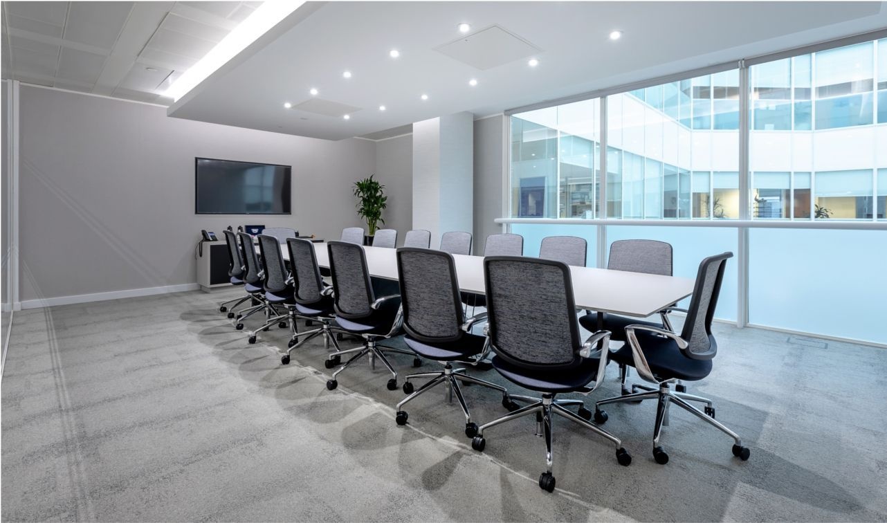 An office boardroom table, surrounded by chairs and a television attached to the wall.