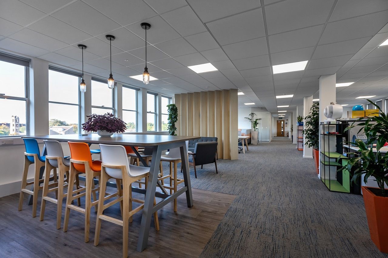 An empty office with desks and workspaces on the right and breakout seating areas on the left.