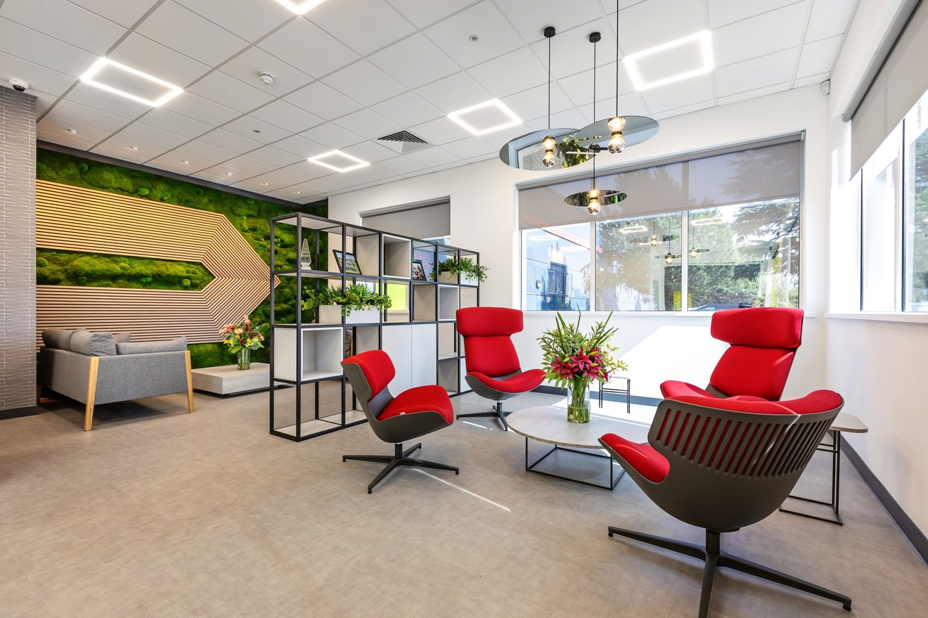 modern office sitting area with flowers large windows and red soft backed chairs and grey sofas