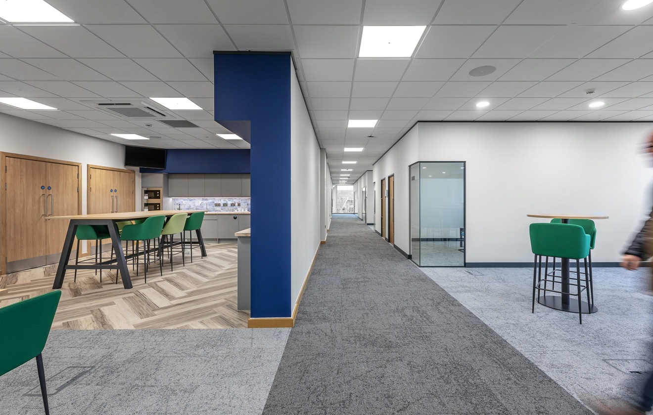 office corridor with kitchen area with green chairs and lounge area to the right