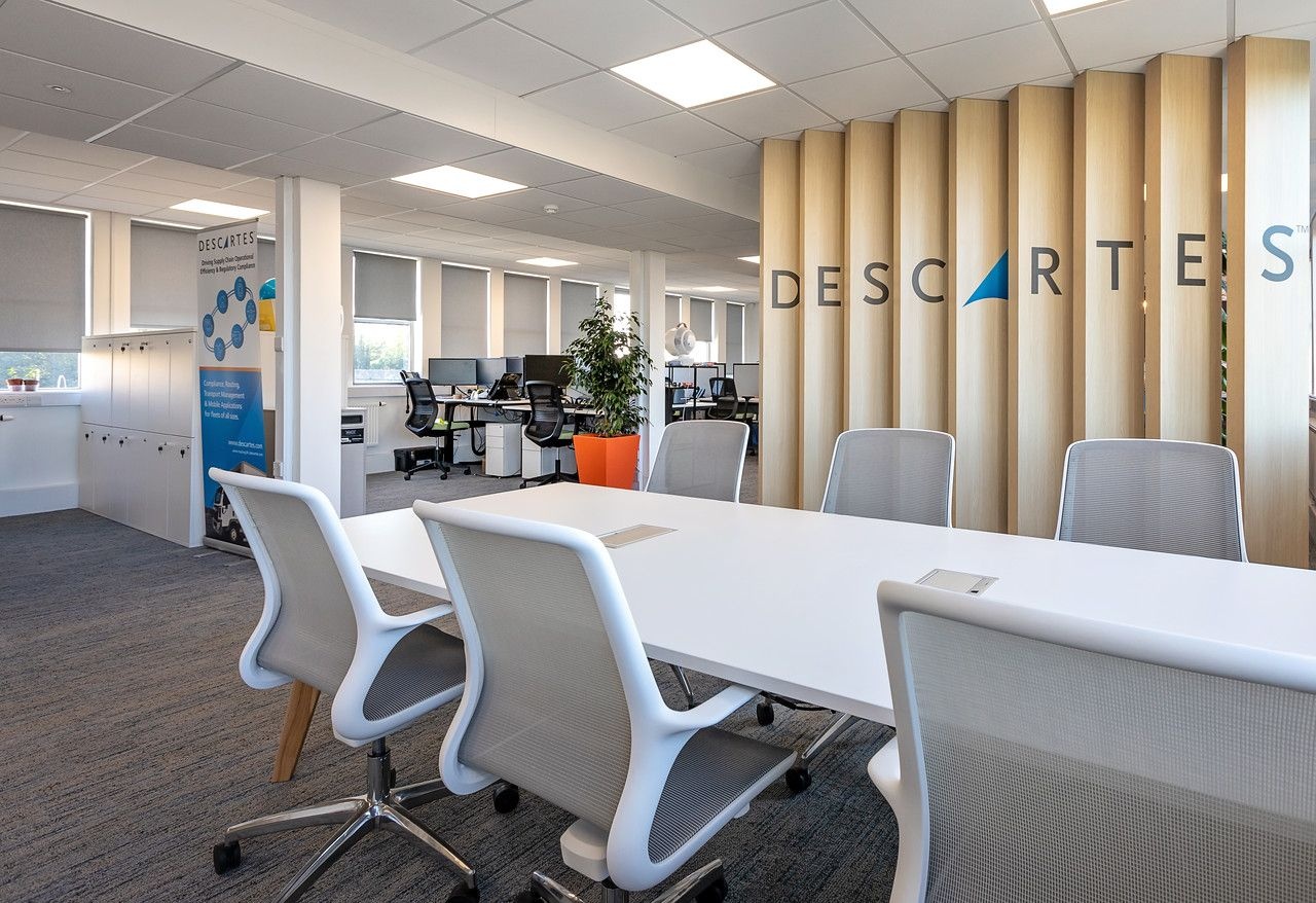 A white table with what and grey chairs surrounding it, with an empty office space in the background.