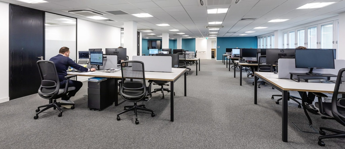 open plan office space with people sat at computer desks with black swivel chairs