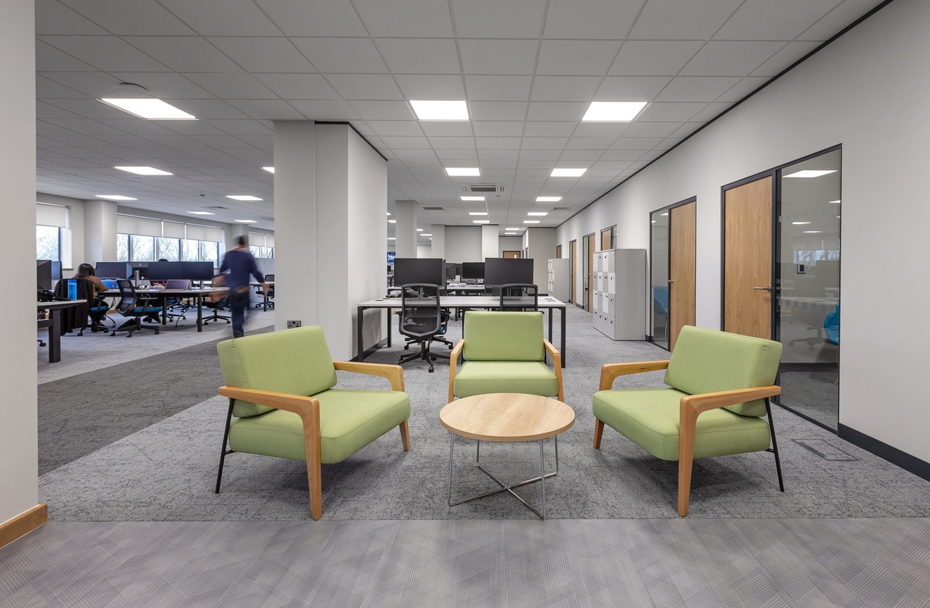 open plan office with compute desks and a sitting area with wooden coffee table and green chairs